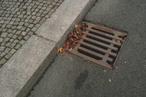 A worker inspects a commercial trench drain grate set in concrete pavement next to parked vehicles.