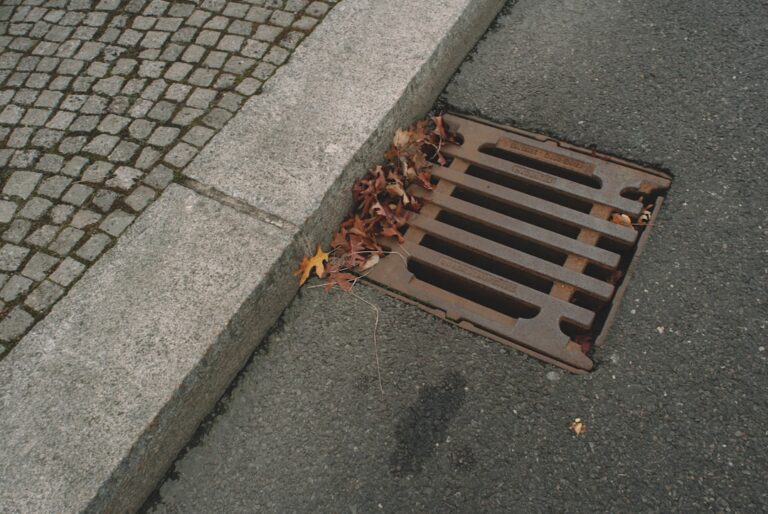 A worker inspects a commercial trench drain grate set in concrete pavement next to parked vehicles.