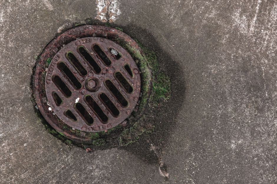 A warehouse worker inspects a trench drain along a concrete floor near loading equipment.