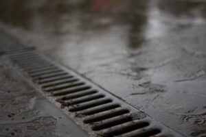 A maintenance worker inspects a trench drain grate at the edge of a commercial parking lot after rainfall