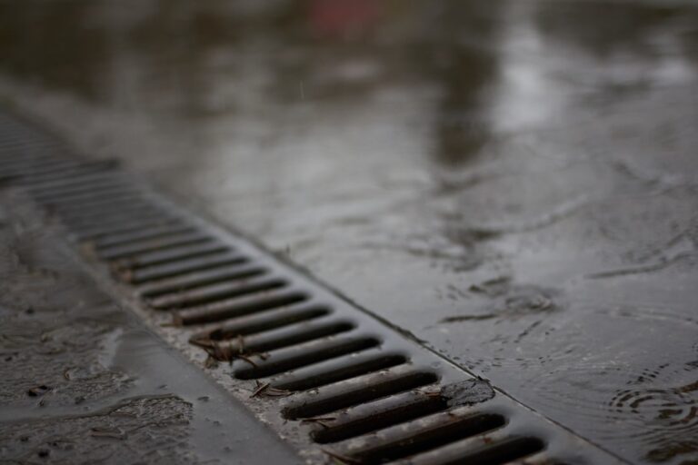 A maintenance worker inspects a trench drain grate at the edge of a commercial parking lot after rainfall