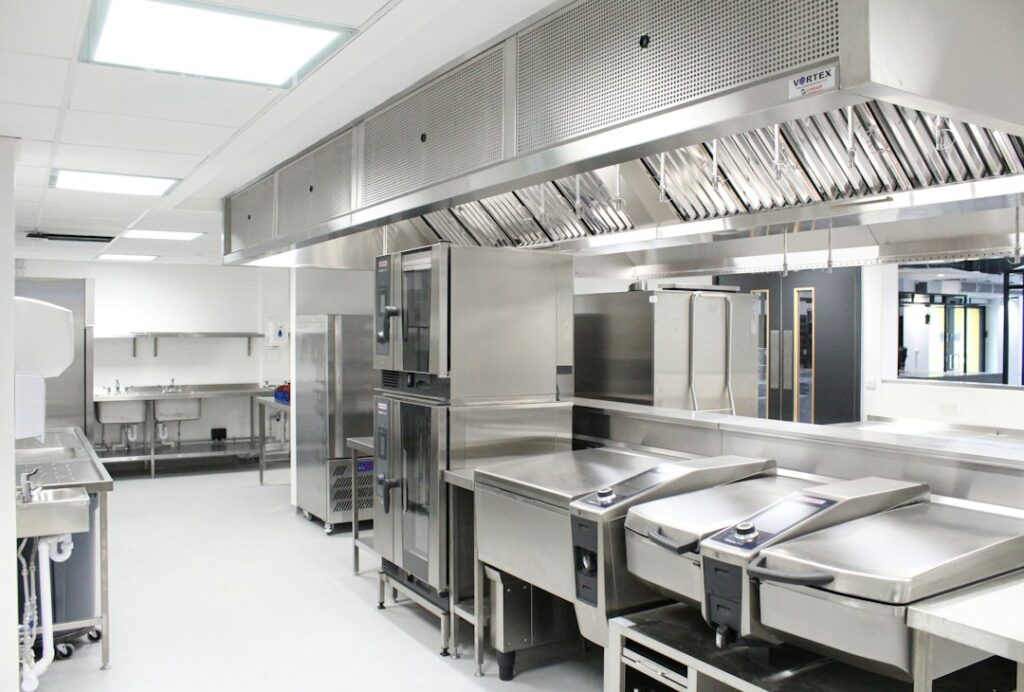 Stainless steel trench drain collecting wash water beside food processing equipment on a clean sloped floor.