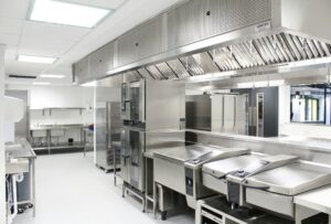 Stainless steel trench drain collecting wash water beside food processing equipment on a clean sloped floor.