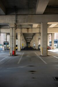 Trench drain crossing a parking garage ramp beside parked vehicles and wet concrete.