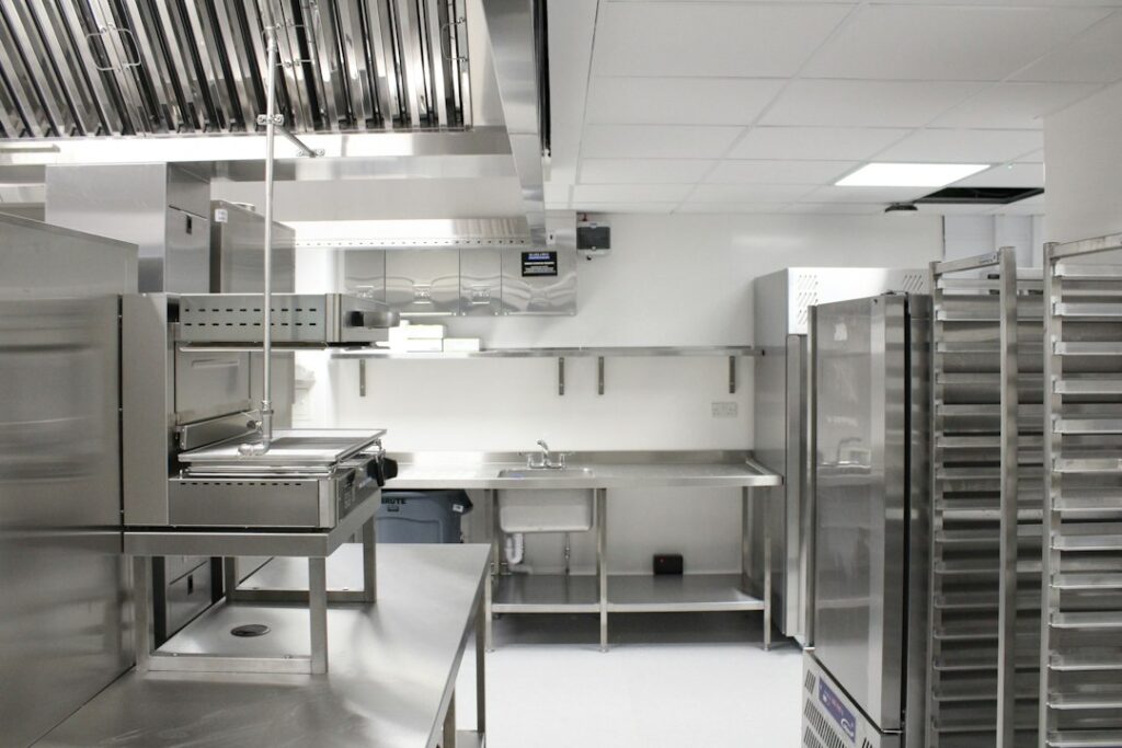 Commercial kitchen workers review floor drains and sloped flooring beside stainless steel equipment.