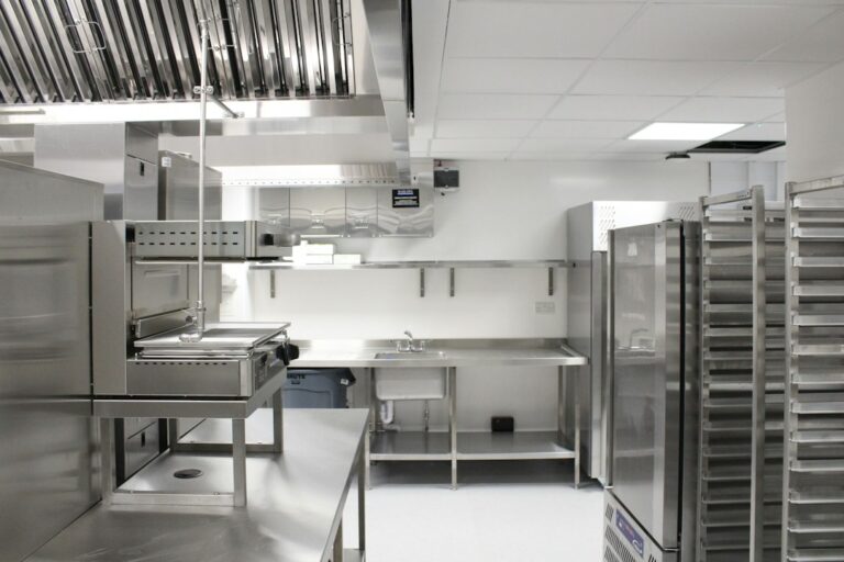 Commercial kitchen workers review floor drains and sloped flooring beside stainless steel equipment.